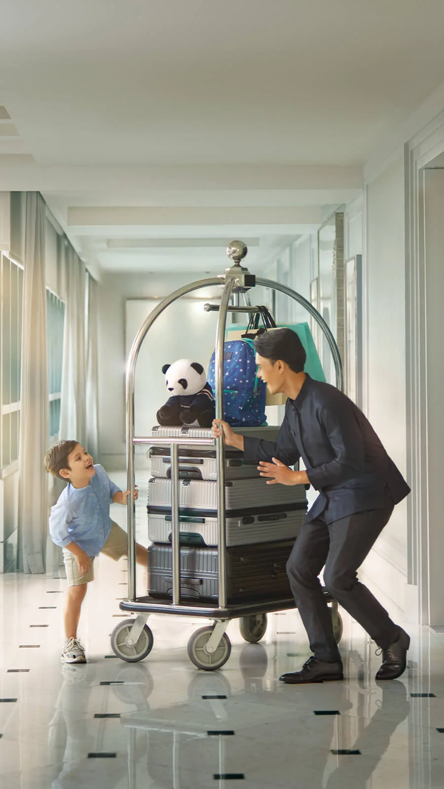 A helpful hotel staff member guides a child's luggage through the polished hallway.