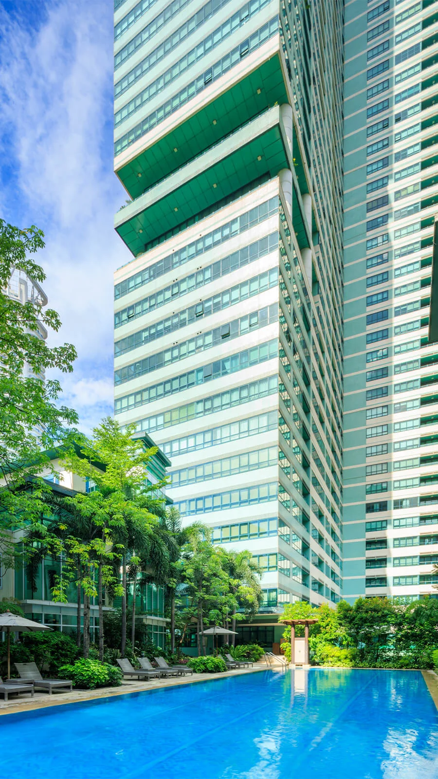 Lush greenery surrounds a sparkling pool, nestled between towering modern buildings.