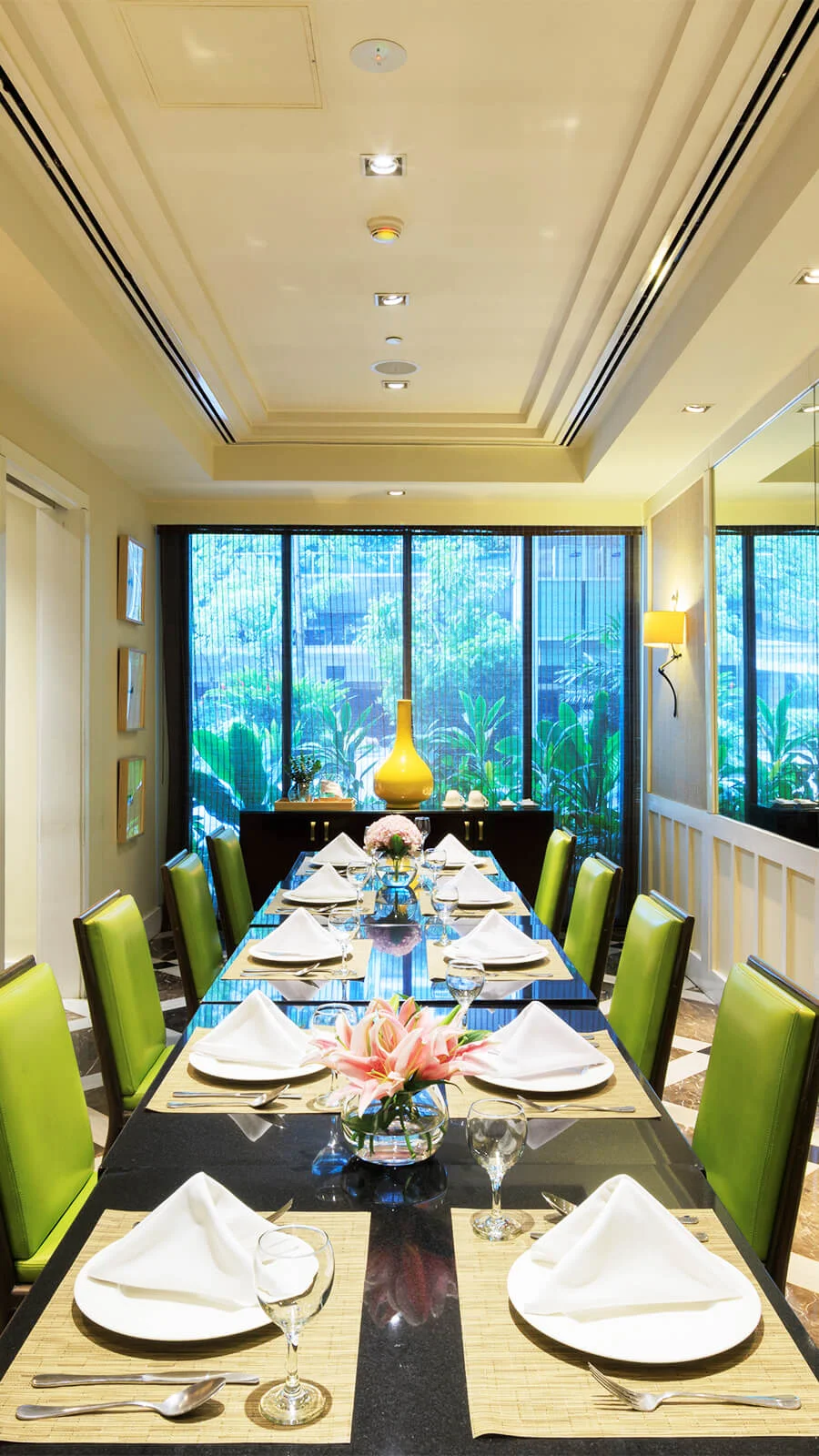 A long banquet table, elegantly set for a gathering, awaits guests in a sun-drenched dining room.