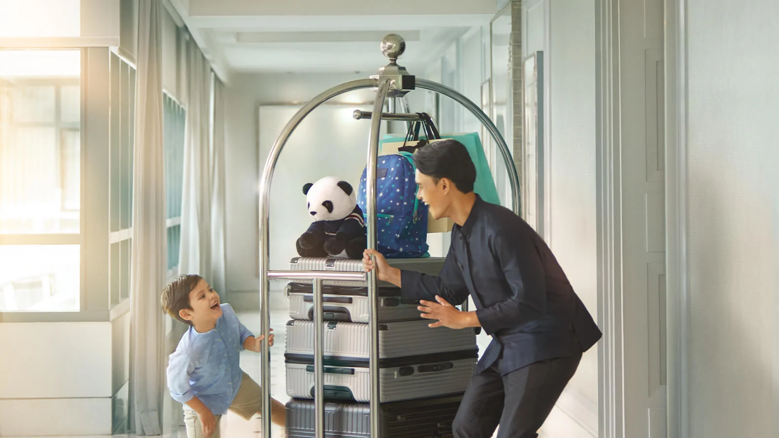 A helpful hotel staff member guides a child's luggage through the polished hallway.